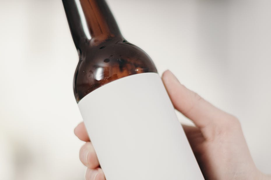 Close-up of a hand holding a blank labeled beer bottle, suitable for mockup in a minimalist home setting.