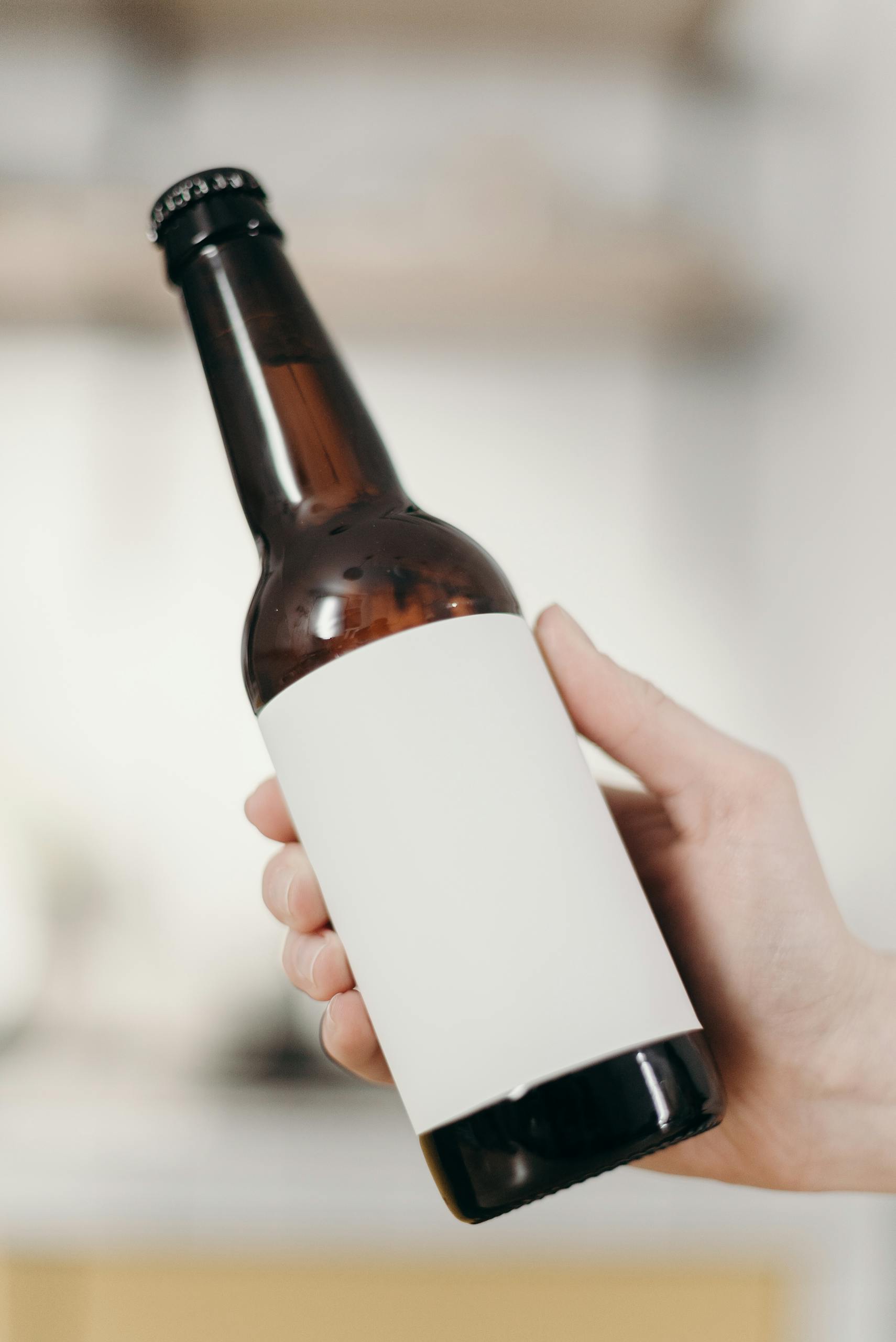 Close-up of a hand holding a blank labeled beer bottle, suitable for mockup in a minimalist home setting.